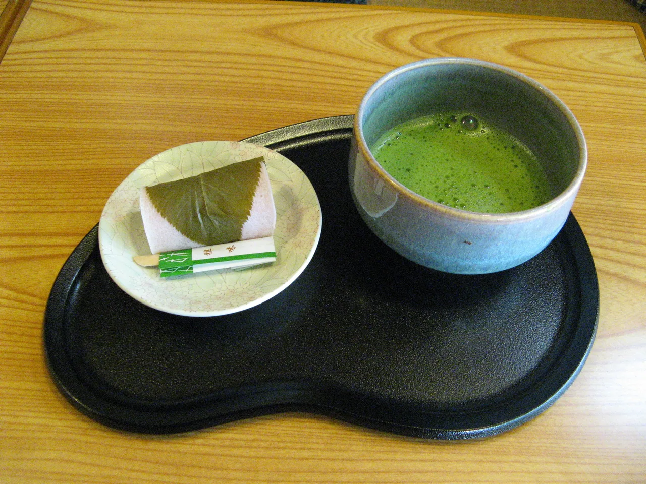 Prepared matcha in a bowl beside a Japanese sweet.
